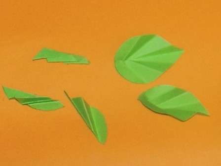 Herefter begynder du at lave bladene. For at gøre dette har du brug for grønt papir. Skær bladet ud, og fold det derefter harmonika for at give en reliefstruktur.